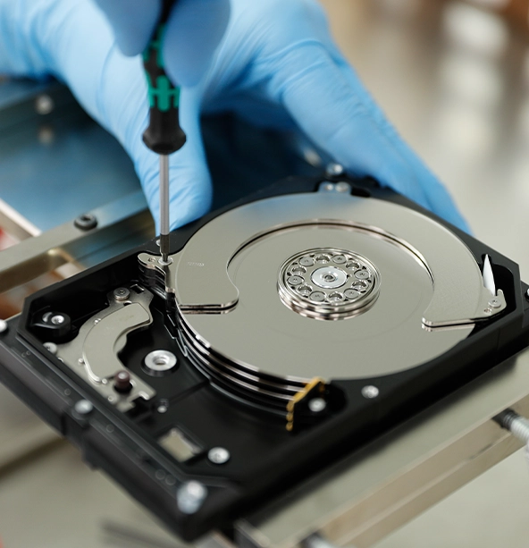 Technician in blue gloves repairing an opened hard drive with exposed platters using a precision screwdriver