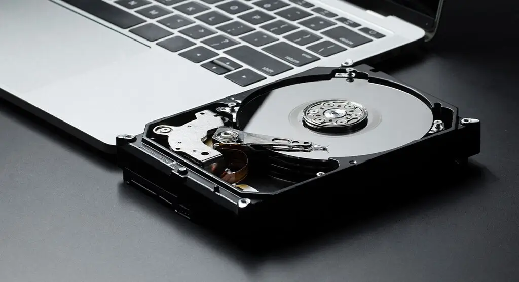 Opened hard disk drive placed next to a silver laptop on a dark surface.