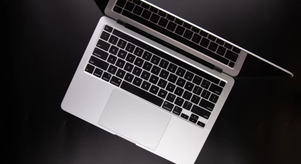 Top view of a partially open silver laptop with black keyboard on a dark surface.