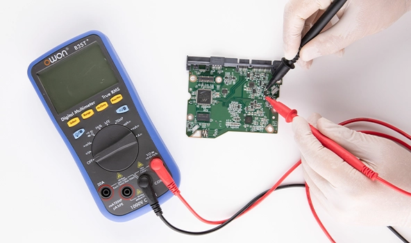 Technician using a digital multimeter to test a hard drive PCB for faults or component-level issues during diagnostics or data recovery.