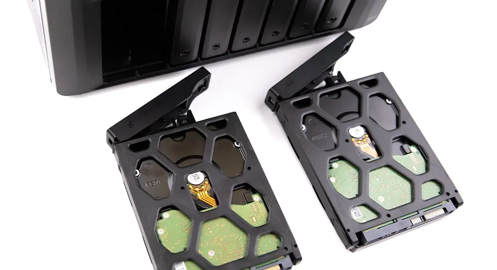 Two internal hard drives in plastic trays placed in front of a multi-bay NAS enclosure with open drive slots