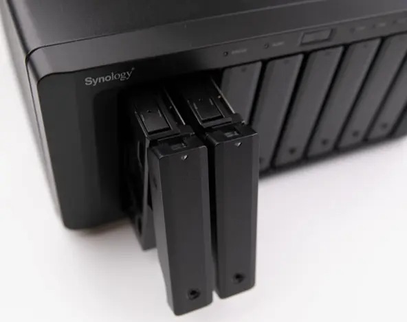 Front-angle view of a Synology NAS unit with two drive bays partially ejected from a multi-bay enclosure.