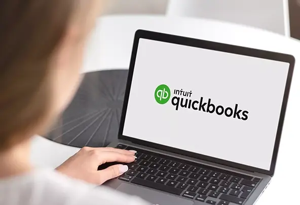 Person using a laptop displaying the Intuit QuickBooks logo on the screen, indicating the launch or login page of the accounting software.
